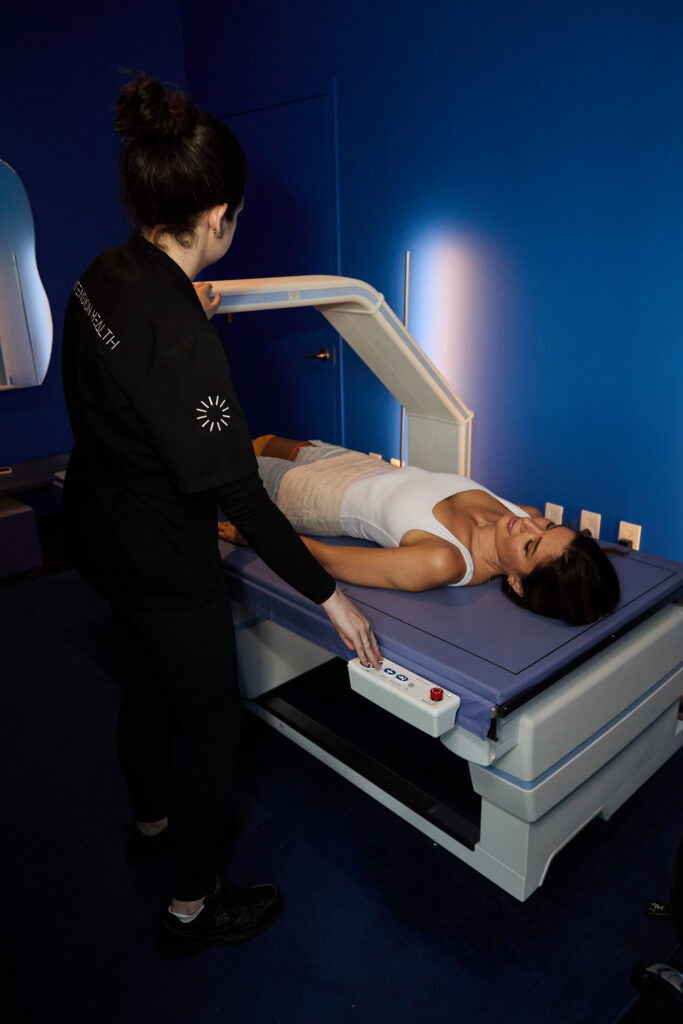 Healthcare professional operating scanning machine with patient lying on exam table in blue room