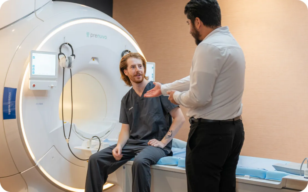 Person in scrubs sits at MRI entrance speaking with someone in business attire.
