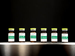 Six labeled glass vials with green caps displayed against a dark background.