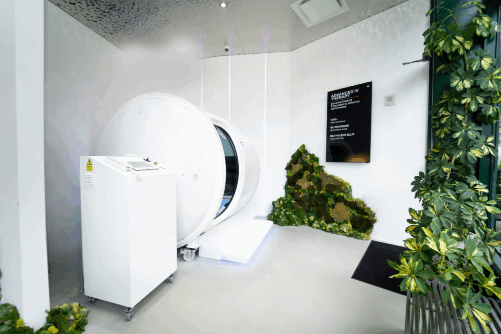 Modern room with cylindrical pod, greenery, and IV therapy sign listing NAD+, glutathione, methylene blue.