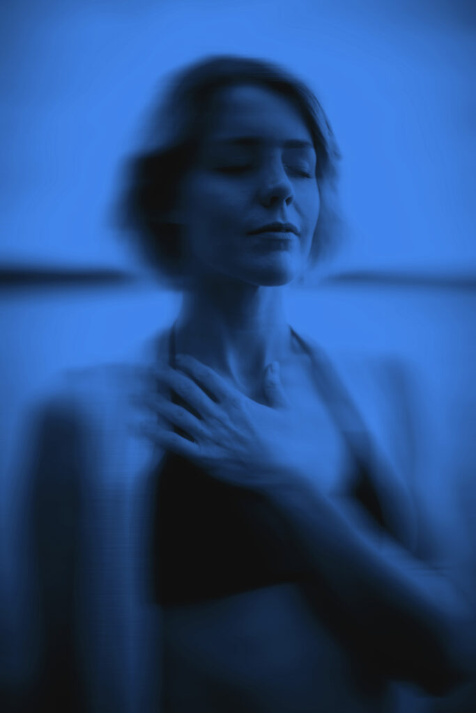 Blurred blue-toned image of a person with short hair, eyes closed, hand on upper chest.
