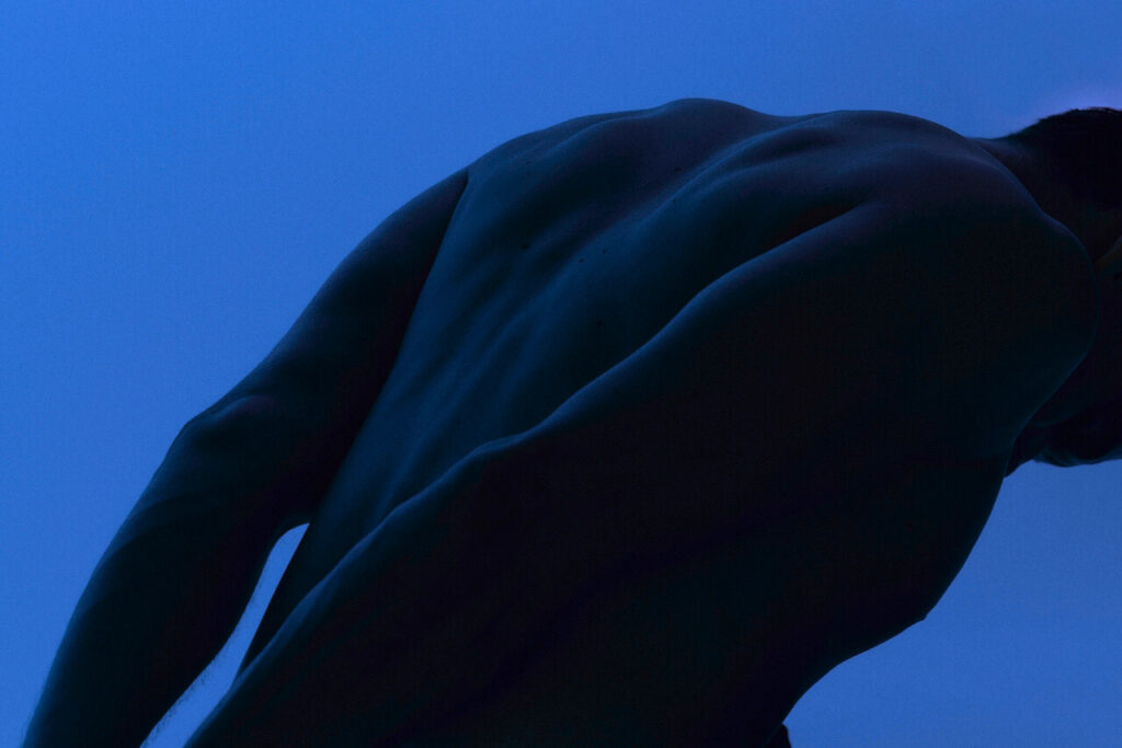 Bare back and arm of a person leaning forward against a clear blue sky background
