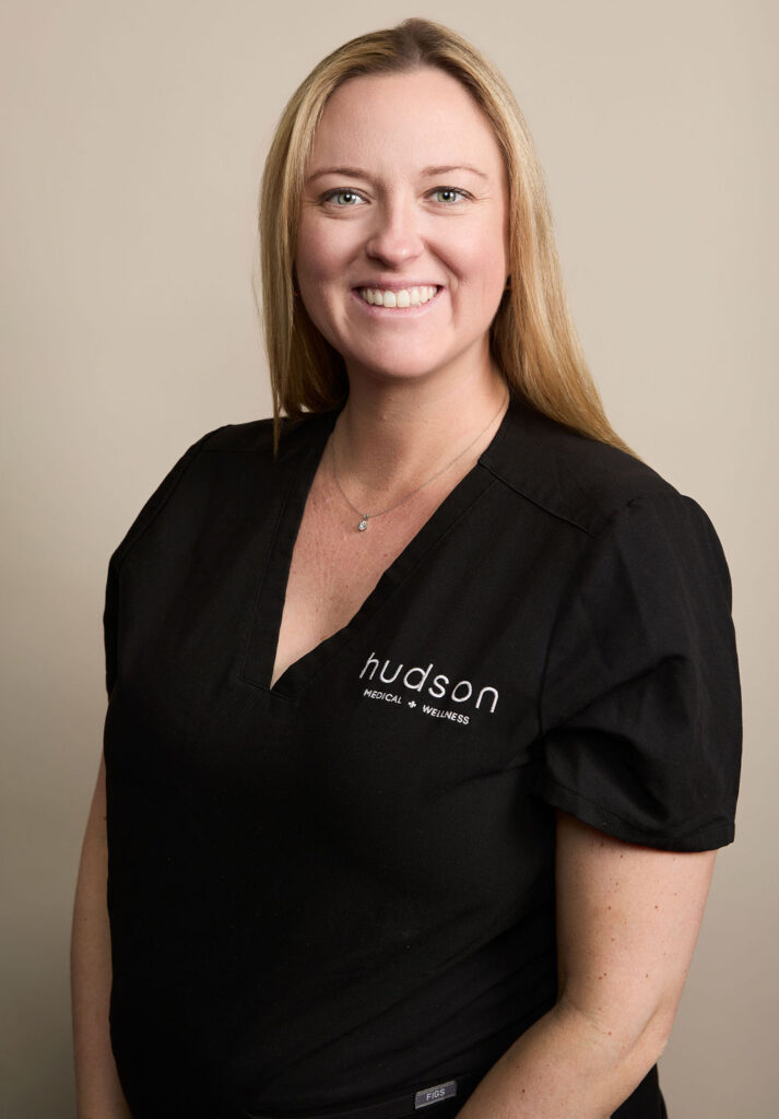 Woman in black Hudson Medical Wellness scrub top smiling on beige background