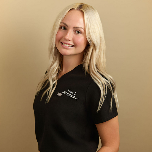 Blonde woman in black medical scrubs smiling against beige background