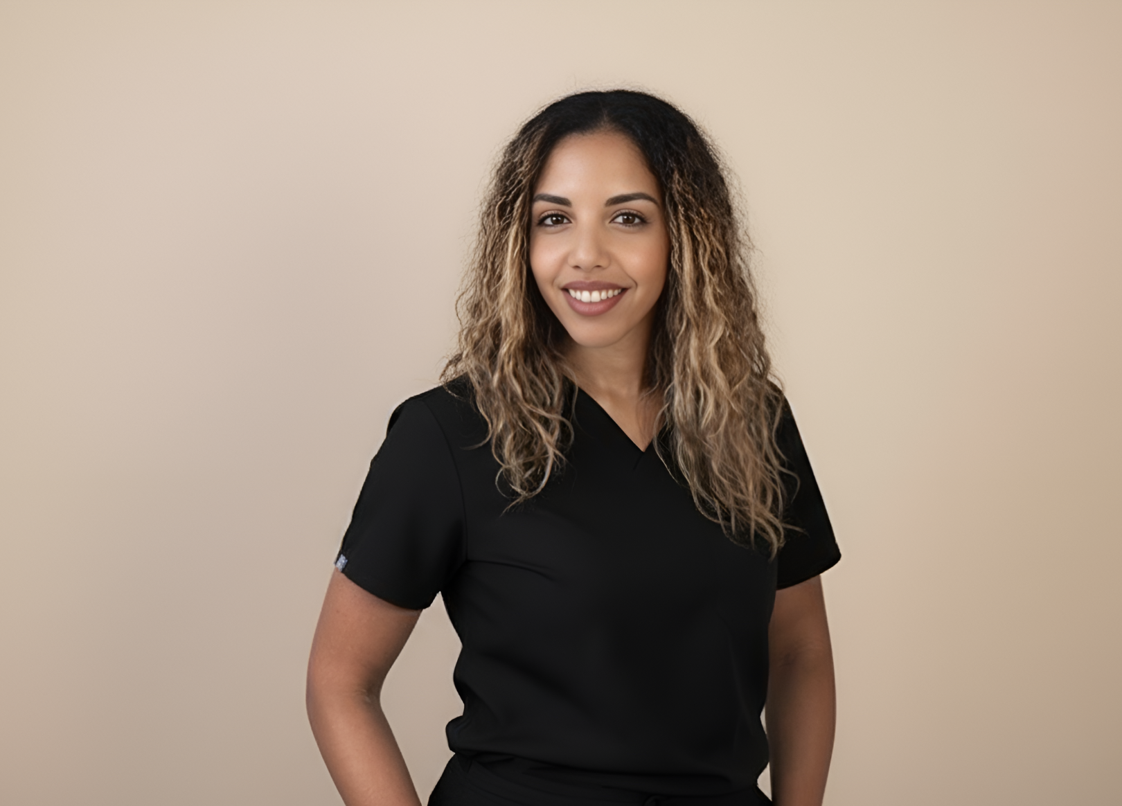 Woman with long curly hair wearing a black short-sleeve top standing against a beige background