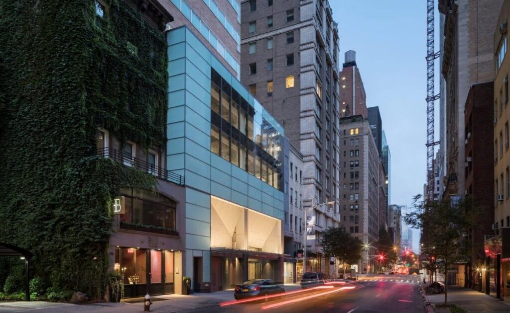 City street at dusk with modern glass building, ivy-covered building, and light traffic.
